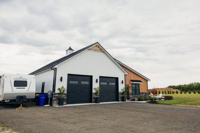 White barn-style pole building with black garage doors and stone accents