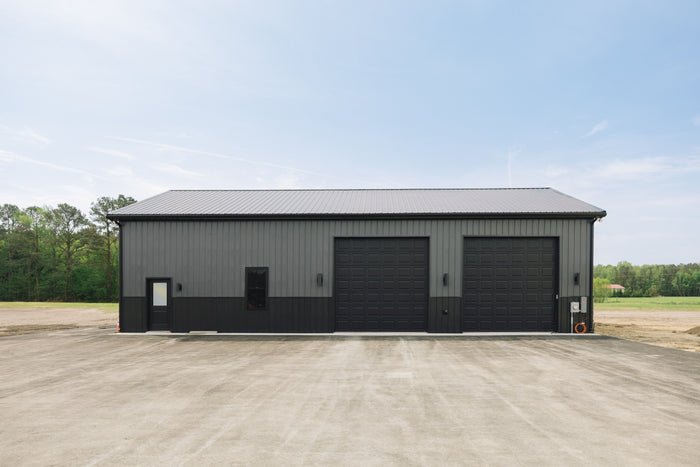 Dark grey steel building with three garage doors on a concrete lot